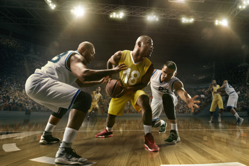 Basketball players playing on court inside a large stadium.