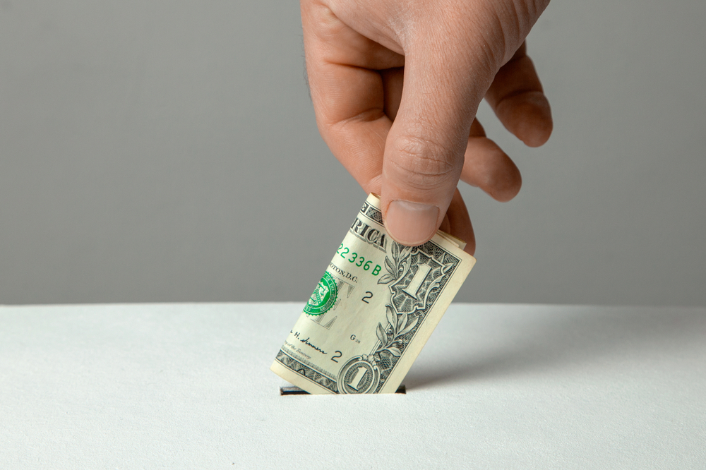 man's hand putting money into donation box slot