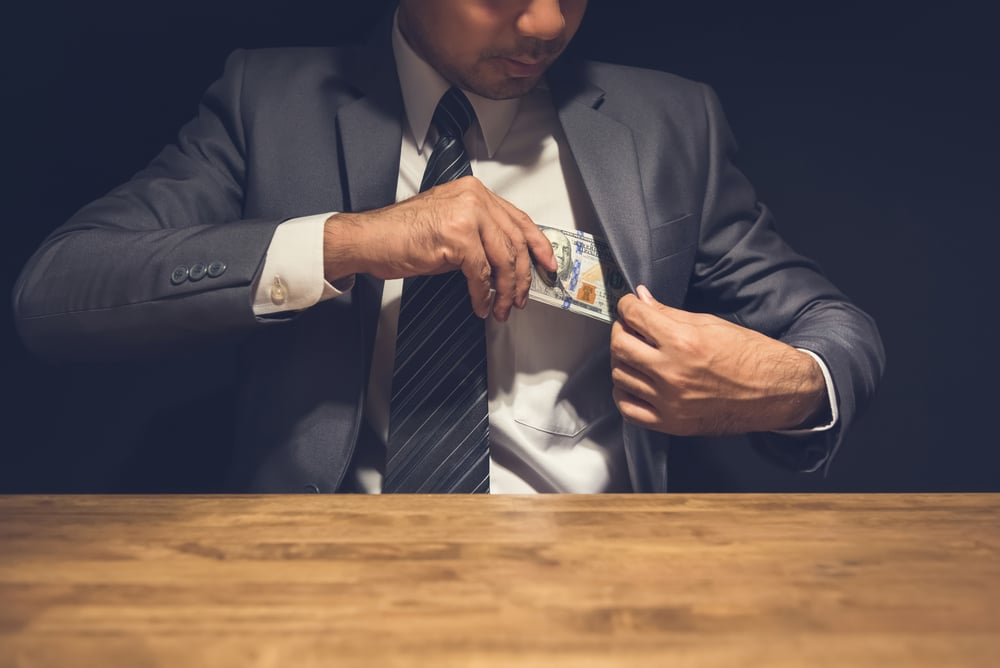 main in suit putting money into his jacket pocket