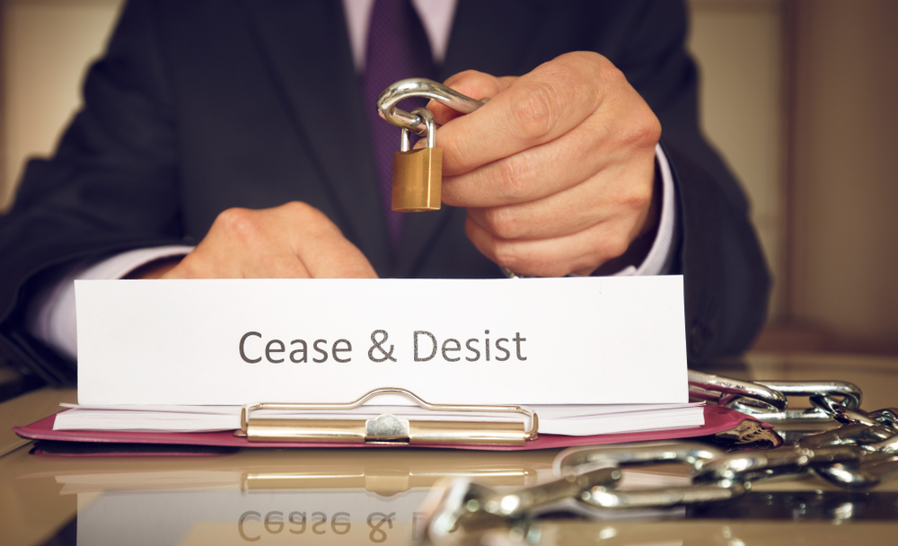 main in suit holds lock and chain with "cease and desist" text on a paper in the foreground