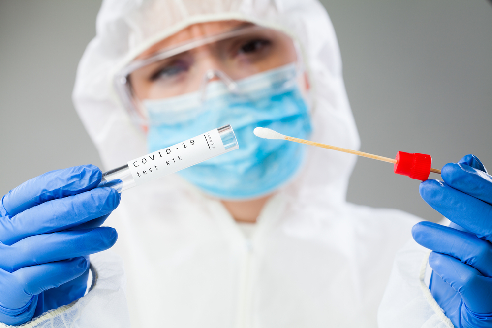 medical professional wearing PPE and holding a COVID-19 swab test