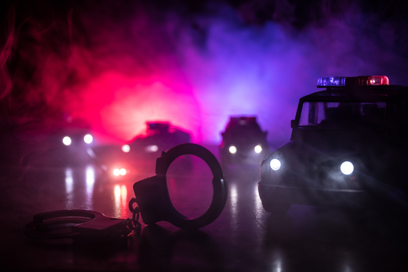 Police cars at night with handcuffs in the foreground