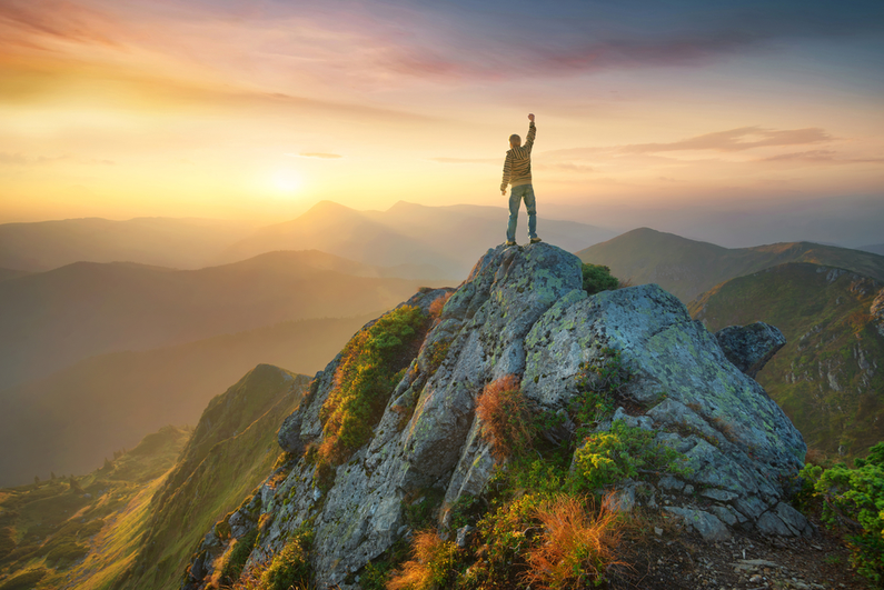 Man standing triumphant on the top of a mountain