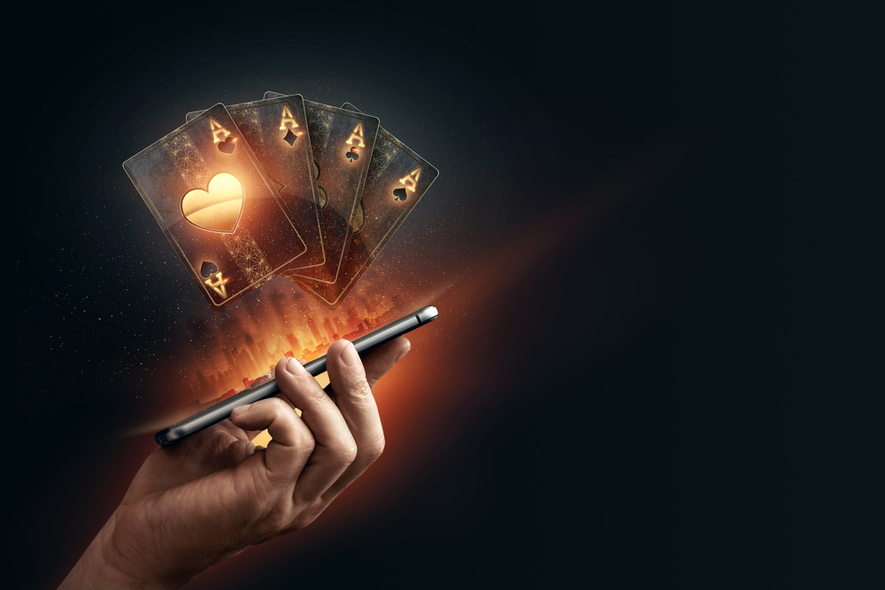 online casino concept with hologram of playing cards hovering above hand holding mobile phone