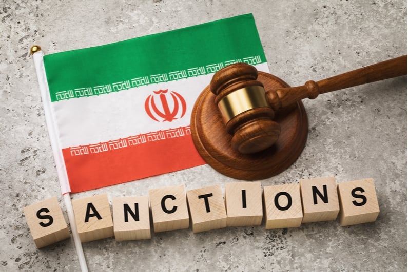 Scrabble blocks spelling out US Sanctions with imagery of Iranian flag and gavel